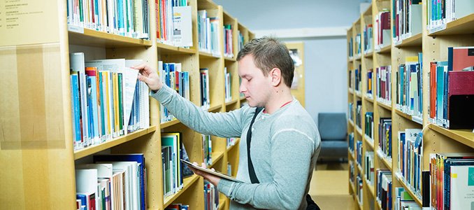 Opiskelija Turun AMK:n kirjaston hyllyjen välissä
