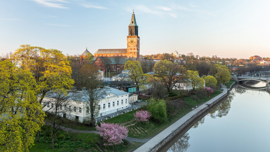 A scenery of the Turku Cathedral and river Aura, with blooming cherry blossom trees.