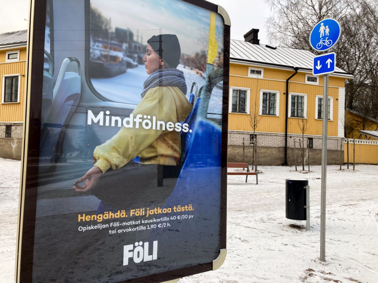 etualalla mainostaulu, jossa Fölin Mindfölness-kampanjan mainos. Taustalla tie ja keltainen puutalo.